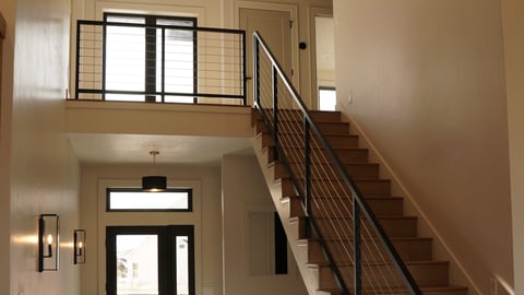 Modern entryway with wooden staircase, metal railing, loft space, and front door with transom window