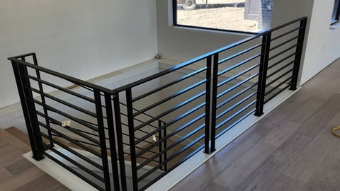 Modern black metal railing with horizontal bars running along an indoor staircase or loft area with wooden flooring