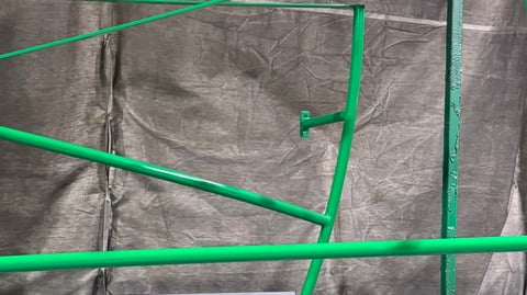 Bright green plastic pipes and connectors arranged on a textured gray tarp or fabric surface