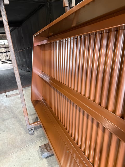 Copper metal corrugated panel display with vertical ribbed texture and horizontal support beams indoors