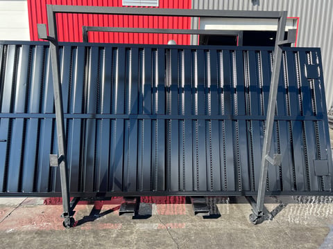 Stack of dark blue corrugated metal panels with red corrugated sheets displayed in background at industrial warehouse